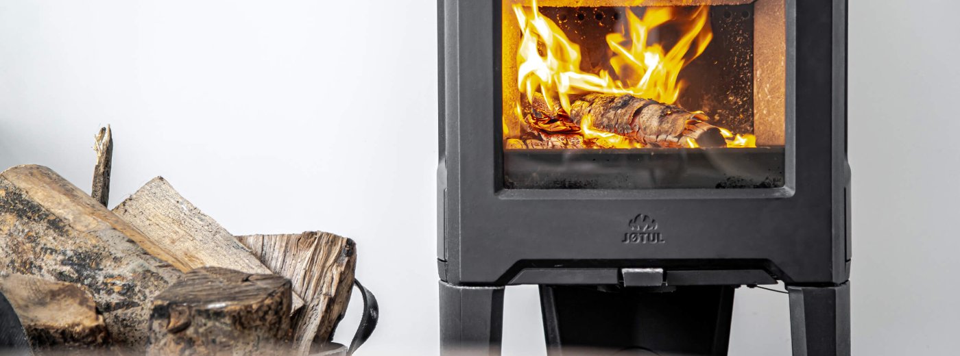 Jøtul F 163 black wood stove with logs on the side and  white wall at the back 