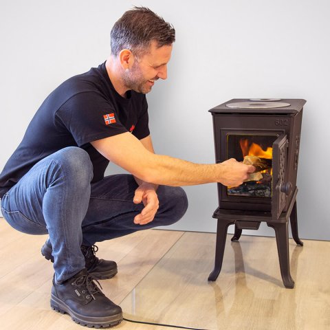 Man adding firewood to his wood stove Jøtul F 602