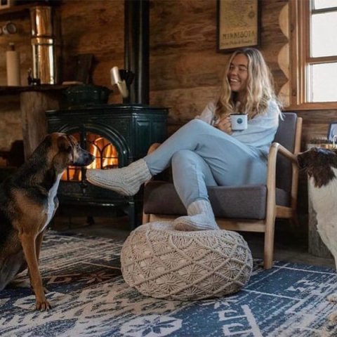 @elylogcabin girl and dog sitting in a chair in front of their wood stove.