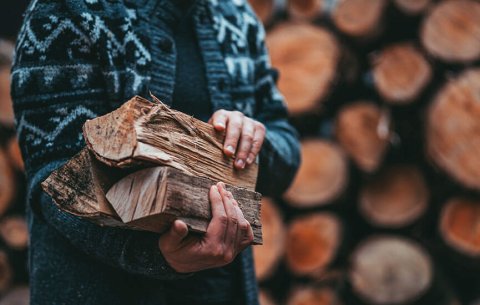 Man in gray knitted sweater carries firewood.